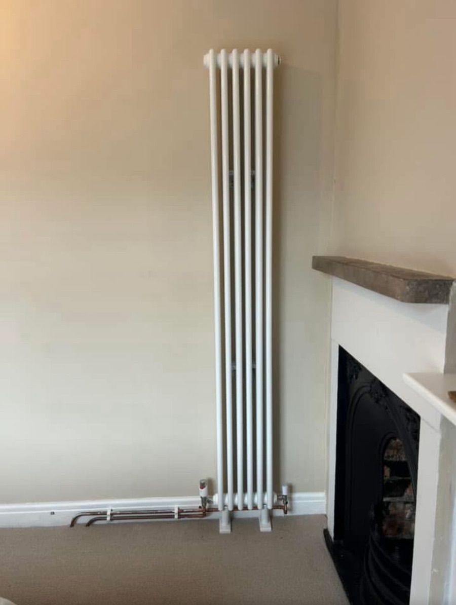 Tall vertical designer radiator fitted beside a fireplace by LR Heating, Leeds