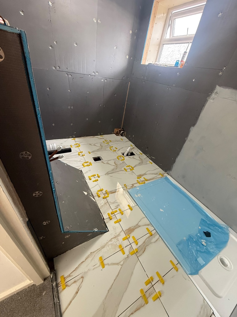 Bathroom floor tiling in progress during a full refit by LR Heating, bath protected in film