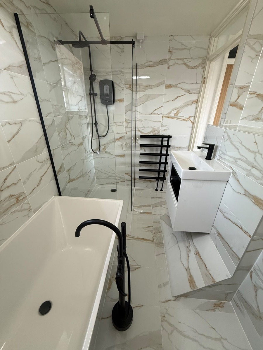 The finished marble-tiled bathroom refit by LR Heating — freestanding bath, walk-in shower and matt-black fittings