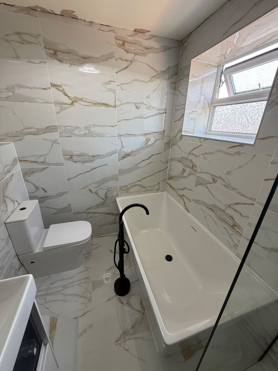 Finished bathroom refit by LR Heating with marble-effect tiles, freestanding bath and black bath filler