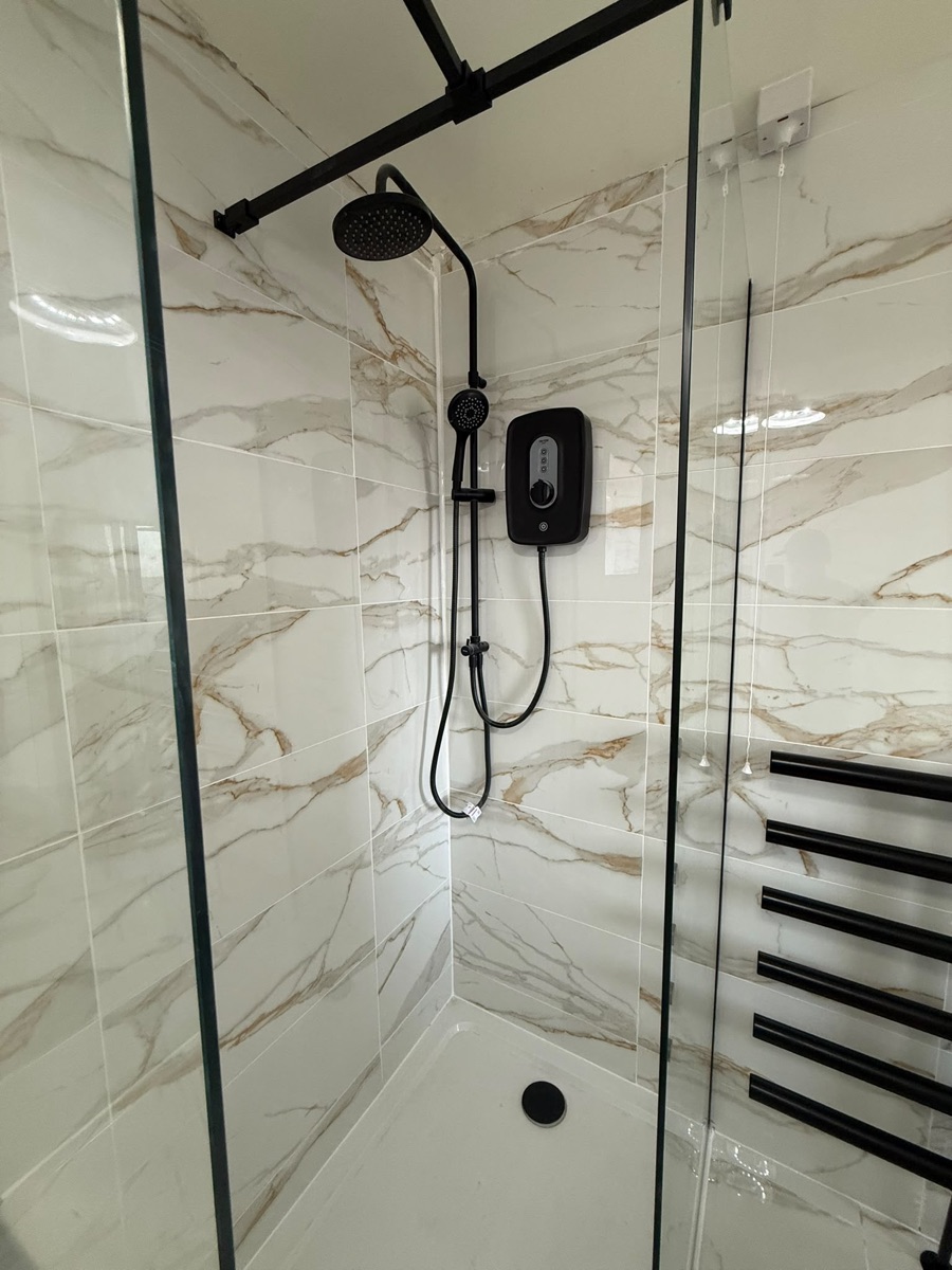 Walk-in shower with matt-black rainfall head and electric shower in a marble-tiled bathroom refit by LR Heating