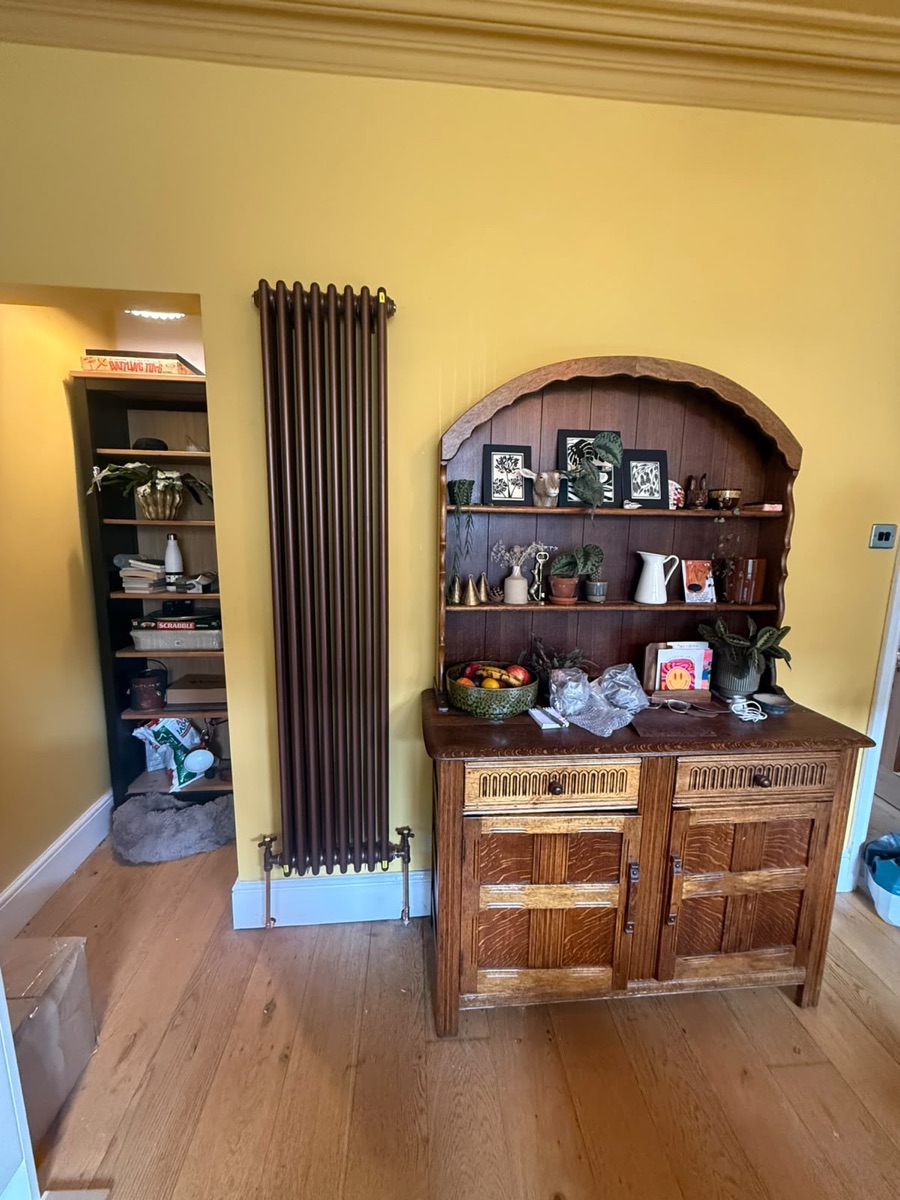 Full-height bronze column radiator fitted by LR Heating against a yellow wall in a period home
